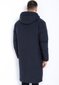 Mann trägt einen langen, dunkelblauen gepolsterten Mantel mit Kapuze, von hinten gegen einen schlichten weißen Hintergrund gezeigt.