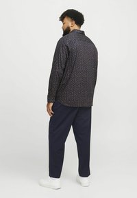 Chemise à manches longues bleu marine avec un petit motif floral, dotée d'un col ouvert et d'une coupe décontractée, assortie à un pantalon sombre et des baskets blanches.
