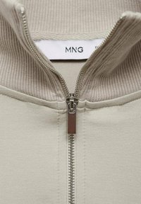 Giacca beige con zip, colletto a coste, dotata di zip metallica e etichetta MNG all'interno. Tessuto morbido con una consistenza liscia.
