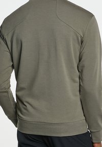 Sudadera verde oliva con mangas largas, cuello redondo y tejido texturizado. Cuenta con un dobladillo entallado y detalles en la costura del hombro.