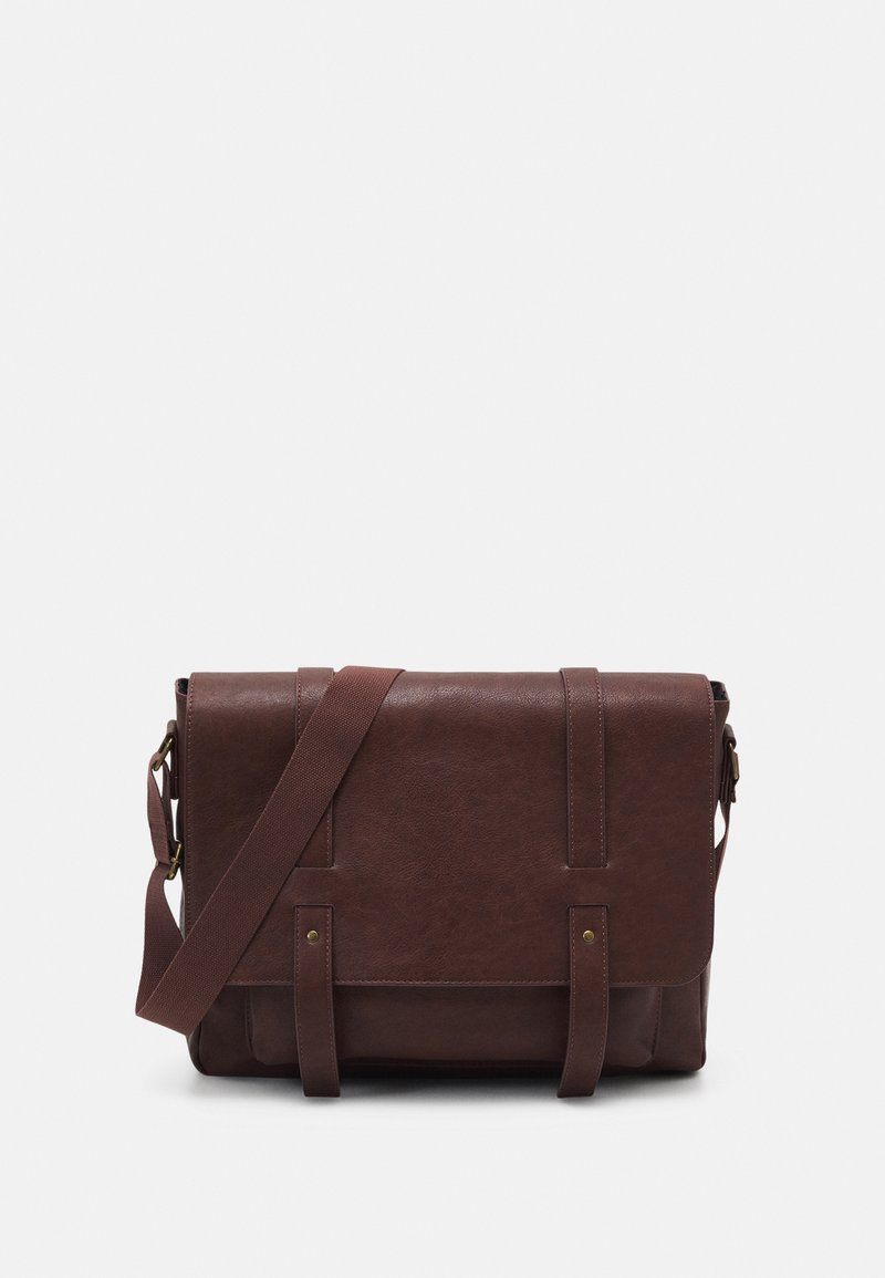 Sac messager en cuir marron foncé avec fermeture à rabat, deux accents de sangle et une bandoulière réglable sur fond uni.