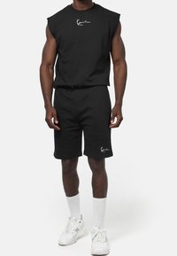 Conjunto deportivo negro compuesto por una camiseta sin mangas y pantalones cortos, fabricado en algodón, con un detalle del logo en blanco en ambas prendas.