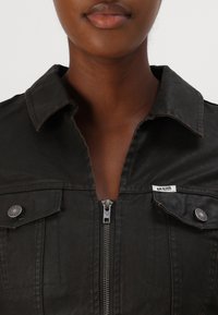 Svart denimjacka med dragkedja fram, spetsig krage och två bröstfickor. Har silverdetaljer och en liten varumärkesetikett på kragen.