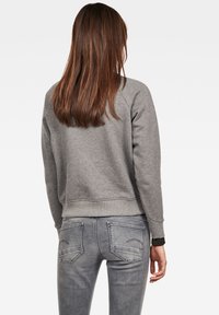Sudadera gris con puños y dobladillo acanalados, combinada con jeans gris claro que tienen bolsillos traseros y detalles de costura sutiles.