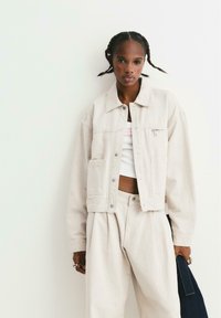 Licht beige denimjack met een kraag, voorzakken en zilveren knopen, gecombineerd met bijpassende hoge taille broek.