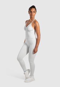 Hvid, tætsiddende atletisk outfit bestående af en rynket top med tynde stropper og matchende leggings, begge lavet af glat, strækbart materiale.