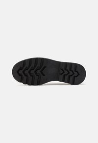 Semelle de chaussure en caoutchouc noir avec des crampons profonds et un motif en zigzag, comportant des accents en relief pour une meilleure adhérence et durabilité.