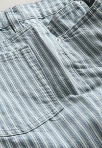 Tissu rayé vertical bleu et blanc montrant un gros plan sur des poches de vêtement et des boutons-pression en métal sur un matériau doux.