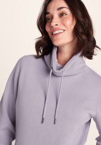 Light purple pullover with a cowl neckline, drawstrings, and a soft, textured fabric. Features relaxed fit and long sleeves.