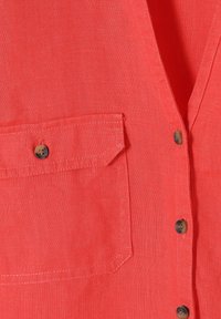 Gros plan sur une chemise en tissu corail avec des boutons et une poche à rabat boutonnée cousue sur le côté gauche.