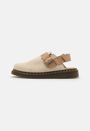 Beige Veloursleder-Sandale mit geschlossenem Zehenbereich, verstellbarem riemen in Hellbraun und schwarzer Gummisohle mit gelber Naht.