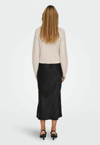 Maglione lavorato a maglia color crema con maniche lunghe, abbinato a una gonna midi in satin nera. Sandali con tacco neri completano l'outfit.