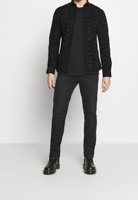 Camicia nera a fantasia di serpente con bottoni, abbinata a una t-shirt nera e pantaloni slim-fit neri. Completano il look degli stivali alla caviglia in pelle nera.