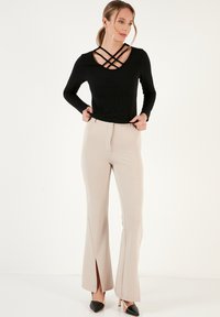 Top nero a maniche lunghe con dettaglio incrociato sul collo, abbinato a pantaloni beige aderenti con fessure laterali. Scarpe nere con tacco.