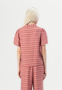 Rød og hvit mønstret topp med korte puffermer, rund halsutskjæring og et geometrisk diamantdesign. Glatt stoff med en avslappet passform.