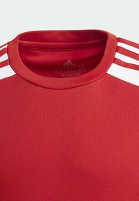 Rød sportsbluse lavet af glat stof. Har rund halsudskæring og tre hvide striber på skuldrene. Etiket angiver størrelse og materiale.