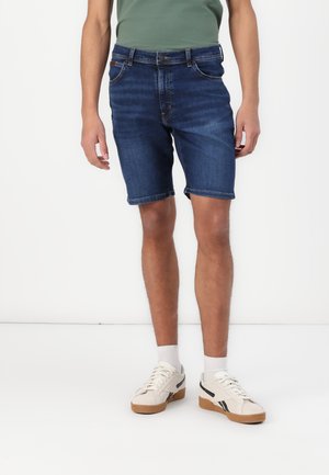Shorts en denim bleu foncé avec une coupe classique, ourlets roulés et poches avant, associés à des baskets blanches et des chaussettes de cheville.