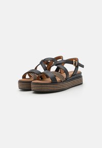 Sandales en cuir noir avec des lanières entrecroisées, dotées d'une semelle compensée tressée et d'une boucle de cheville réglable.