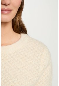 Cremefarbener Pullover mit einem strukturierten, rautenförmigen Strickmuster und einem runden Ausschnitt. Zeigt einen weichen Stoff mit einem leicht flauschigen Aussehen.