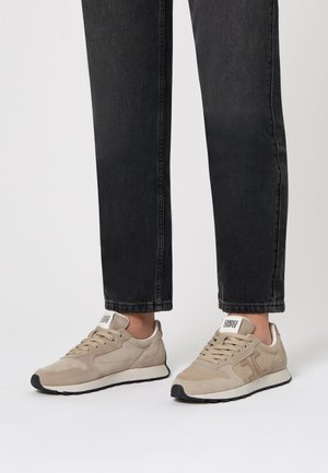 Sneakers in suede beige chiaro con suola bianca e sottili accenti neri a contrasto. Presentano un design con lacci e un logo sulla linguetta.