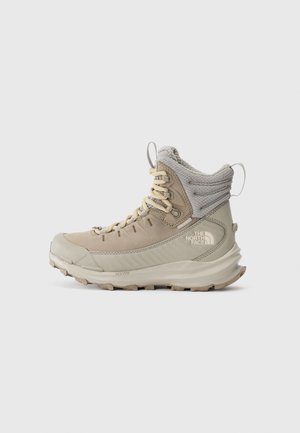 Beige og grå høyhælte tursko med polstret ankelkrage, robust såle og The North Face-logo på siden.