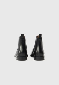 Černé kožené kotníkové boty s hladkým povrchem, kulatými špičkami a malými zadními poutky. Mají nízký sloupkový podpatek a minimalistické švy.