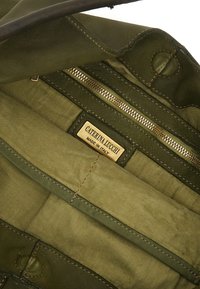 L'interno verde in pelle di una borsa presenta una tasca con zip e un'etichetta dorata che recita "Caterina Lucchi - Made in Italy" con dettagli di cucitura.