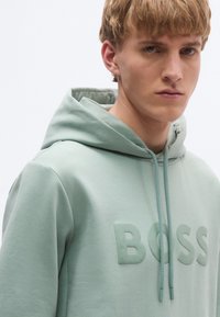 Μέντα πράσινο φούτερ από απαλό βαμβάκι, με ανάγλυφο λογότυπο "BOSS" στο μπροστινό μέρος, κουκούλα με κορδόνι και άνετη εφαρμογή.