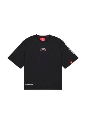 T-shirt nera a maniche corte con piccola grafica di bocca di squalo sul petto, "LIVE A LIFE OF FREEDOM" sulla manica destra e "THE JOURNEY BEGINS" in basso a sinistra.