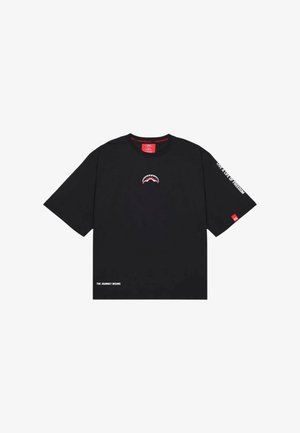 T-shirt nera a maniche corte con piccola grafica di bocca di squalo sul petto, "LIVE A LIFE OF FREEDOM" sulla manica destra e "THE JOURNEY BEGINS" in basso a sinistra.