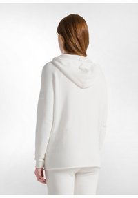 Sudadera blanca con capucha, de manga larga, suave al tacto y con un corte relajado. Presenta una costura en la parte posterior y puños acanalados, combinada con pantalones a juego.