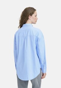 Light blue long-sleeve shirt with white vertical stripes, curved hem, buttoned cuffs, and a classic collar, made from a smooth fabric.