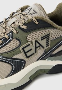 Adidași atletici bej și verde măsliniu cu panouri din plasă, accente texturate negre și logo-ul EA modelat. Dispun de șireturi solide și talpă groasă.