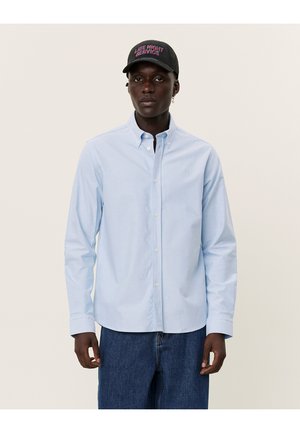Light blue button-up shirt with long sleeves and a soft cotton texture, paired with a black cap featuring "Late Night Service" embroidery.