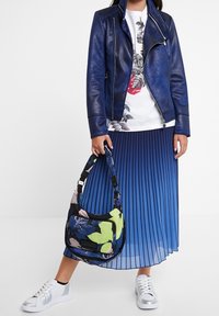 Niebieska skórzana kurtka motocyklowa, biała koszulka z kwiatowym wzorem, plisowana spódnica w niebieskim gradiencie, kwiatowa torba oraz metaliczne srebrne sneakersy.
