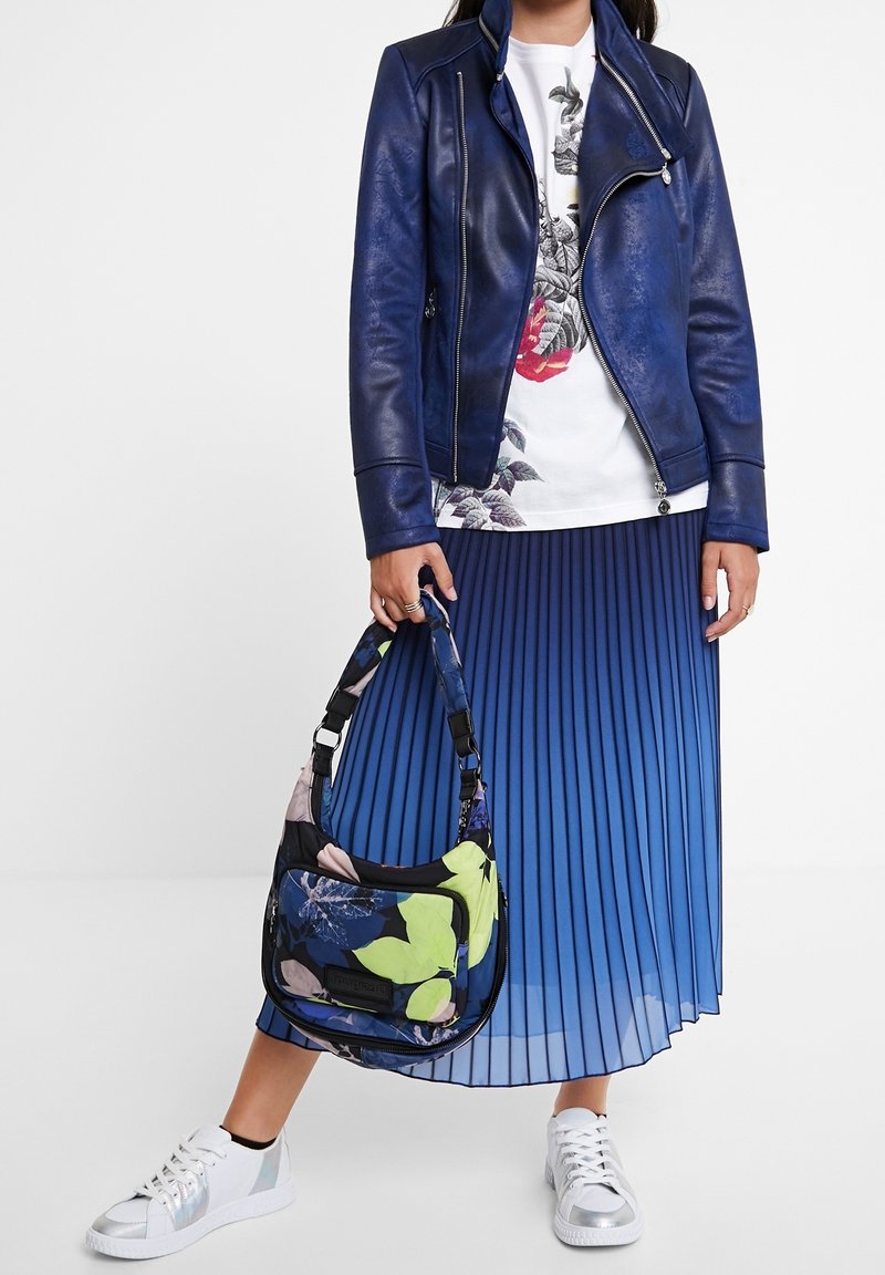 Niebieska skórzana kurtka motocyklowa, biała koszulka z kwiatowym wzorem, plisowana spódnica w niebieskim gradiencie, kwiatowa torba oraz metaliczne srebrne sneakersy.