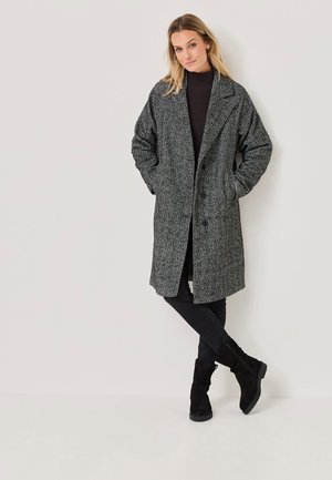 Manteau long gris avec un motif texturé, larges revers et deux poches avant. Assorti à un jean noir et des bottes noires à l'allure décontractée.