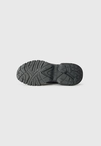 Semelle de chaussure en caoutchouc noir avec un motif de semelle texturé, comportant des rainures profondes pour l'adhérence et un design ergonomique. Bords lisses et construction robuste.