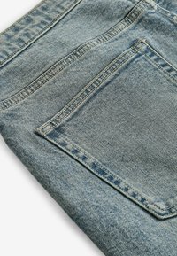 Jean en denim bleu avec une surface texturée, doté d'une poche arrière et de surpiqûres contrastantes le long des coutures. Plié sous un angle.