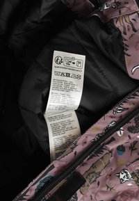 Zorglabel binnenin een zwart en roze jas met natuurthema patronen, waarop de stofsamenstelling, wasinstructies en een recycling symbool zijn weergegeven.