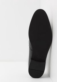 Chaussure en cuir noir avec un motif crocodile, présentant un bout lisse et rond ainsi qu'une semelle en caoutchouc plate. Taille 42 indiquée sur la semelle.