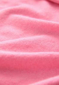 Rožnata tkanina z mehko, teksturirano površino, ki se lepo ovija v nežne gube, kar prikazuje gladek zaključek in subtilen sijaj.