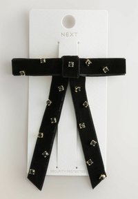 Black velvet hair accessory with a center tie and two trailing ends, embellished with square gold-accented black gems. Attached to a white card.