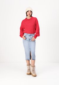 Röd stickad tröja, ljusblå denimkjol med slits fram, och beigefärgade stövlar med pälsfoder. Modellen bär en krämfärgad mössa.