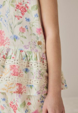 Child's arm beside light-colored floral dress with lace trim and small round metal tag on fabric.