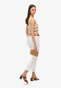 Crème haak top met multicolore strepen, gecombineerd met witte rechte jeans. Bruine met hakken sandalen en een geweven handtas.