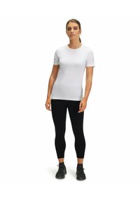T-shirt bianco con maniche corte e scollo rotondo, abbinato a leggings neri. Dettagli notevoli includono sottili accenti sulle spalle.