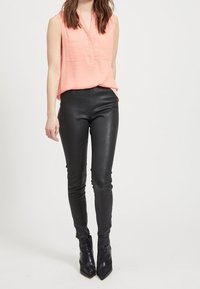 Blouse rose sans manches avec un col en V et deux poches avant, associée à un pantalon noir en similicuir et des bottines noires à bout pointu.