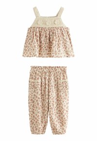 Tvådelad barnklädsel med en blommönstrad, krämfärgad crop top med flätade axelremmar och ett matchande par byxor med elastisk midja och fickor.