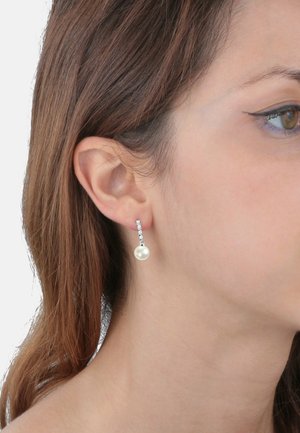 Orecchini a goccia con perla bianca e una catena decorativa in argento, con una linea dritta di piccoli dettagli trasparenti, indossati all'orecchio di una modella.